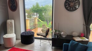 Una sala de estar moderna con un amplio ventanal corredizo que da a un balcón, un sofá negro, un tapete rojo y una mesita con adornos.