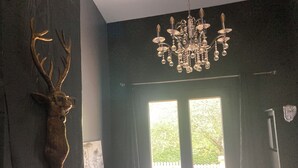 Habitación con cabeza de venado montada, una araña y vista al exterior a través de una puerta.