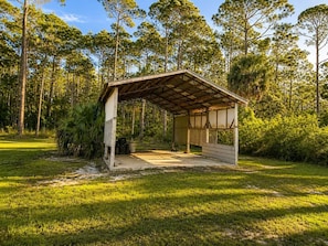A covered outdoor area with a bench, surrounded by trees and grass.