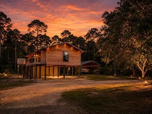 Una cabaña de madera con terraza, rodeada de árboles, durante el atardecer.