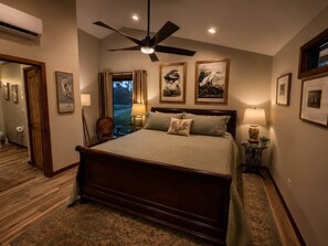 A bedroom with a large bed, a ceiling fan, and framed artwork on the walls.