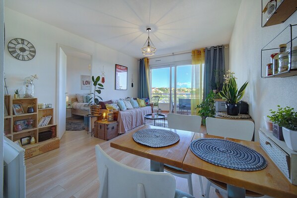 A spacious living area with a wooden dining table, a sofa, and a balcony with a view.