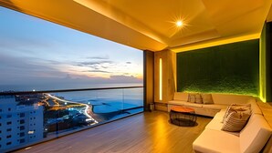 A modern living room with a balcony overlooking a cityscape and water at sunset.