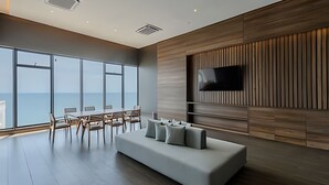 A spacious room with a large window overlooking the sea, a modern sofa, and a flat-screen TV mounted on the wall.