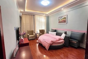Hotelkamer met een rond bed, een tafeltje, twee stoelen, een televisie en een schilderij aan de muur.