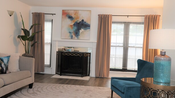 A living room with a sofa, armchair, and a fireplace. There is a large abstract painting on the wall and a potted plant. - Spacious Condo in Southfield, Michigan (Southfield)
