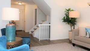 A modern living room with a staircase, a blue armchair, a beige sofa, and a large potted plant. - Spacious Condo in Southfield, Michigan (Southfield)