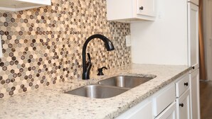 A kitchen with a double sink, white cabinets, and a backsplash with hexagonal tiles. - Spacious Condo in Southfield, Michigan (Southfield)
