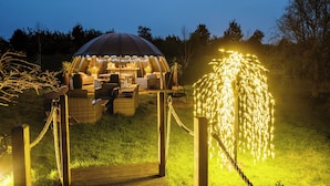 A gazebo with a dome roof and string lights, surrounded by a wooden deck and wicker furniture. - Shepherd's Hut- Hot Tub- Wellness Spa- Wood Burner (Nottingham)