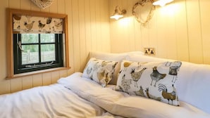 A bedroom with a bed, a window with a curtain featuring bird illustrations, wall-mounted heart-shaped light fixtures, and a wall socket. - Shepherd's Hut- Hot Tub- Wellness Spa- Wood Burner (Nottingham)