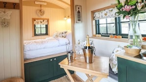 A cozy room with a bed, a table with a bottle and glasses, a window with a view of pumpkins, and a wall with a sign. - Shepherd's Hut- Hot Tub- Wellness Spa- Wood Burner (Nottingham)