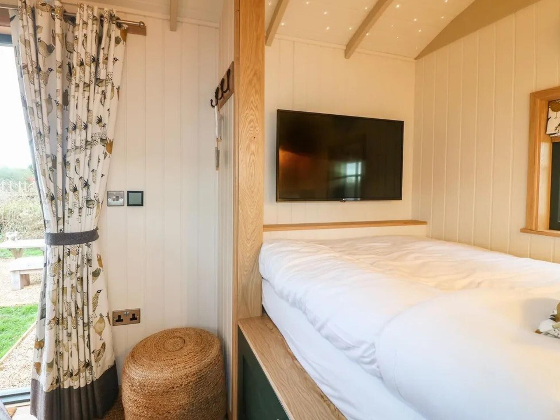 A bedroom with a bed, a television mounted on the wall, and a window with curtains.