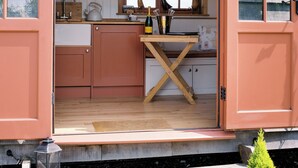 A compact kitchen with wooden cabinets, a sink, and a window with a view. - Shepherd's Hut- Hot Tub- Wellness Spa- Wood Burner (Nottingham)
