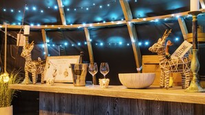 A rustic wooden bar area with string lights, a star decoration, a welcome sign, a framed picture, wine glasses, a candle holder, and a decorative bowl. - Shepherd's Hut- Hot Tub- Wellness Spa- Wood Burner (Nottingham)