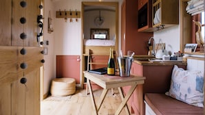 A cozy kitchen with wooden cabinets, a dining table with a bottle of champagne, and a cozy seating area. - Shepherd's Hut- Hot Tub- Wellness Spa- Wood Burner (Nottingham)