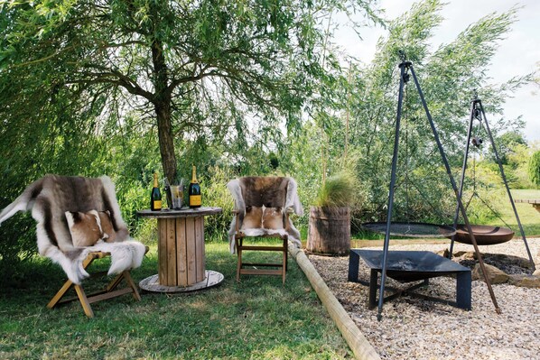 A rustic outdoor seating area with two wooden chairs, a small round table with bottles, and a hanging swing. - Shepherd's Hut- Hot Tub- Wellness Spa- Wood Burner (Nottingham)