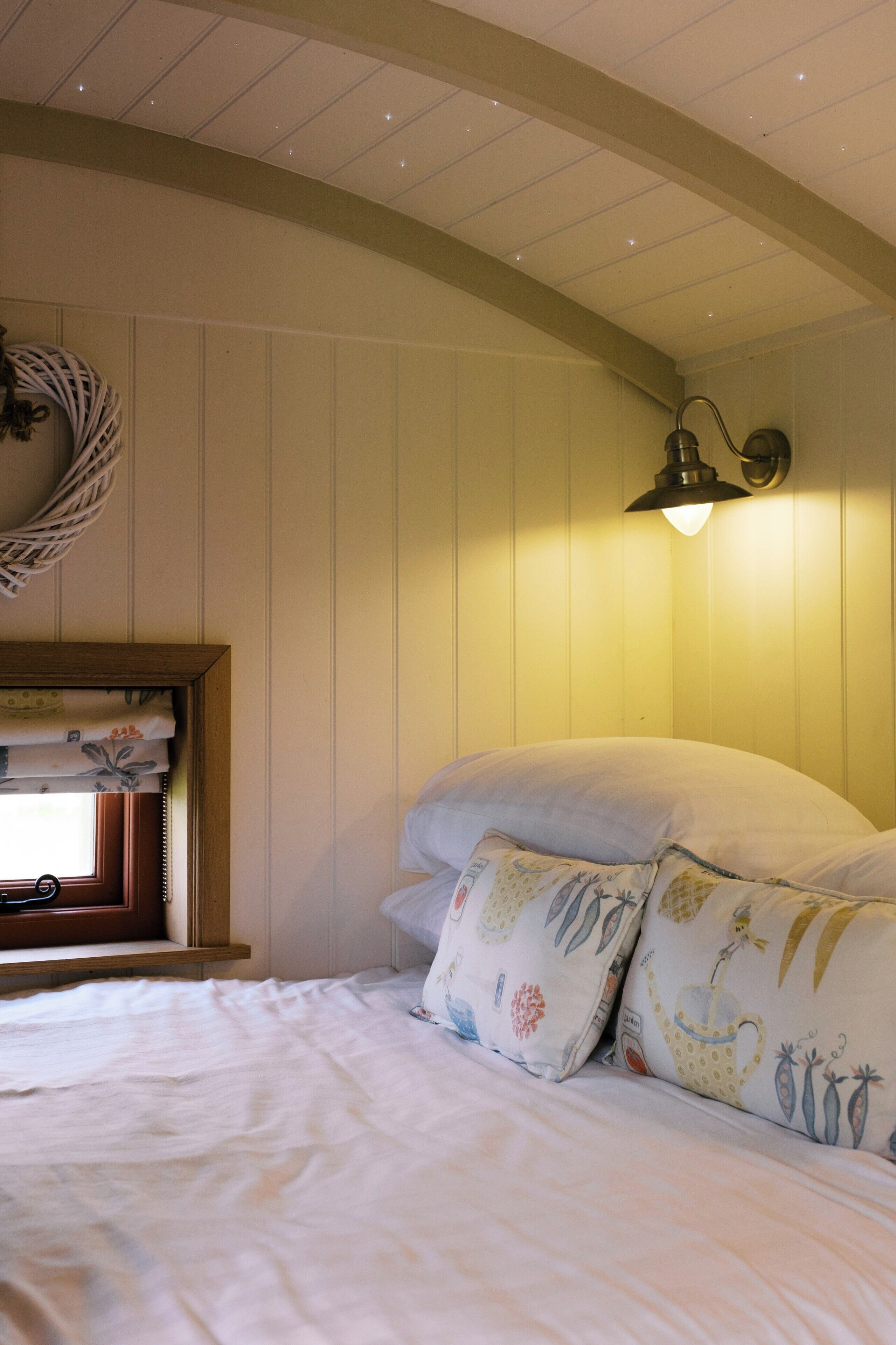 A bedroom with a bed, pillows, a wall-mounted lamp, and a window with curtains.