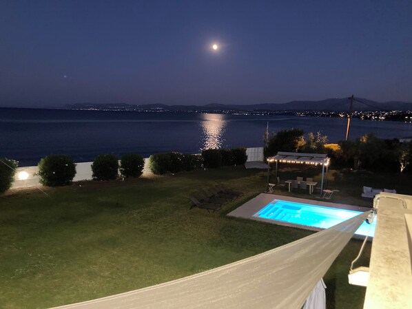 A nighttime view of a pool area with a clear view of the water and a distant cityscape.
