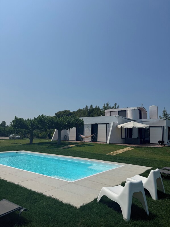 Ein modernes Haus mit Swimmingpool, weißer Gartenmöbel und einer Hängematte.