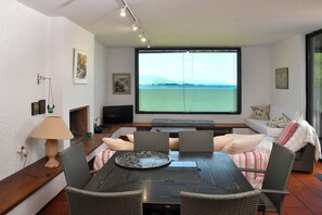 Ein Essbereich mit Tisch, Stühlen, einem Fernseher und einem großen Fenster mit Meerblick.