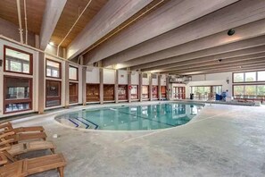 Ein Hallenbad mit Holzliegestühlen, großen Fenstern und hoher Decke.