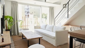 Una sala de estar moderna con un sofá, una mesa de centro y un comedor con sillas. Se ve una escalera que conduce a un nivel superior.