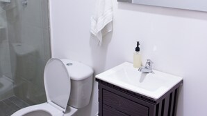 Une salle de bain comprenant des toilettes, un lavabo, un miroir et un espace douche.