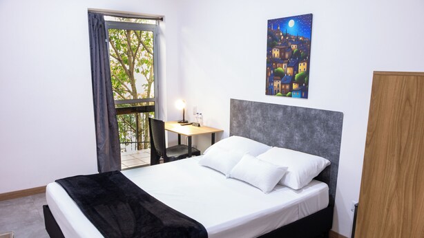 Une chambre d’hôtel avec un lit, un bureau, une chaise, un tableau et une vue sur l’extérieur.