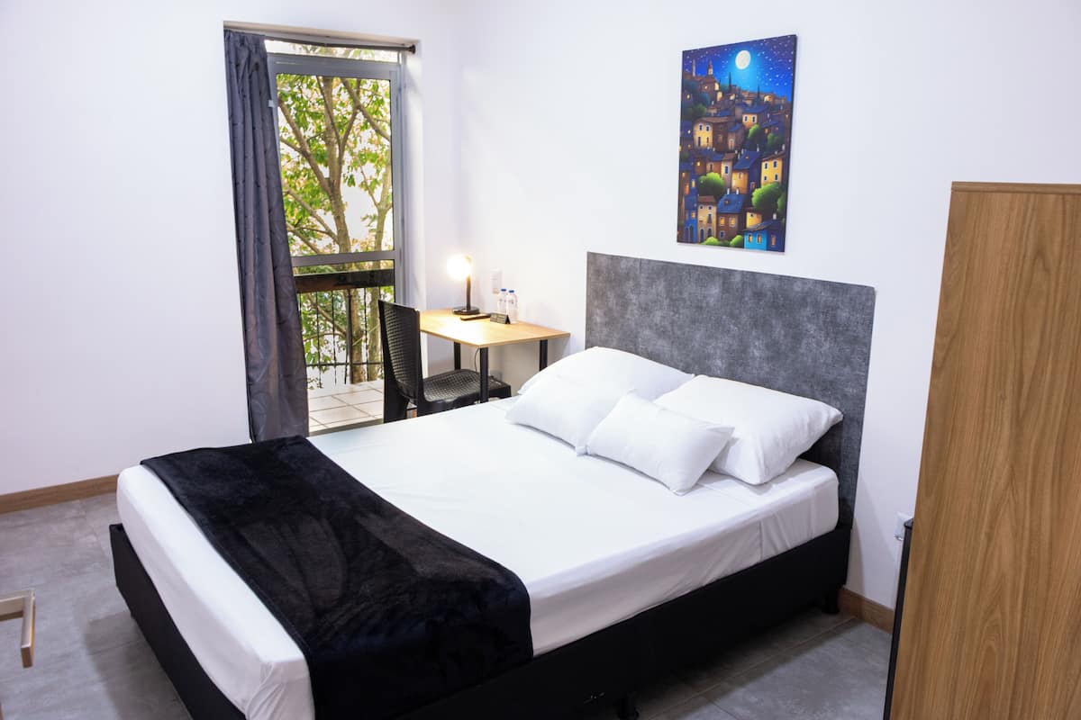 Een hotelkamer met een bed, bureau, stoel, schilderij en uitzicht op het groen.