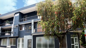 Un immeuble à plusieurs étages, doté de balcons, de grandes fenêtres et d’un arbre devant.