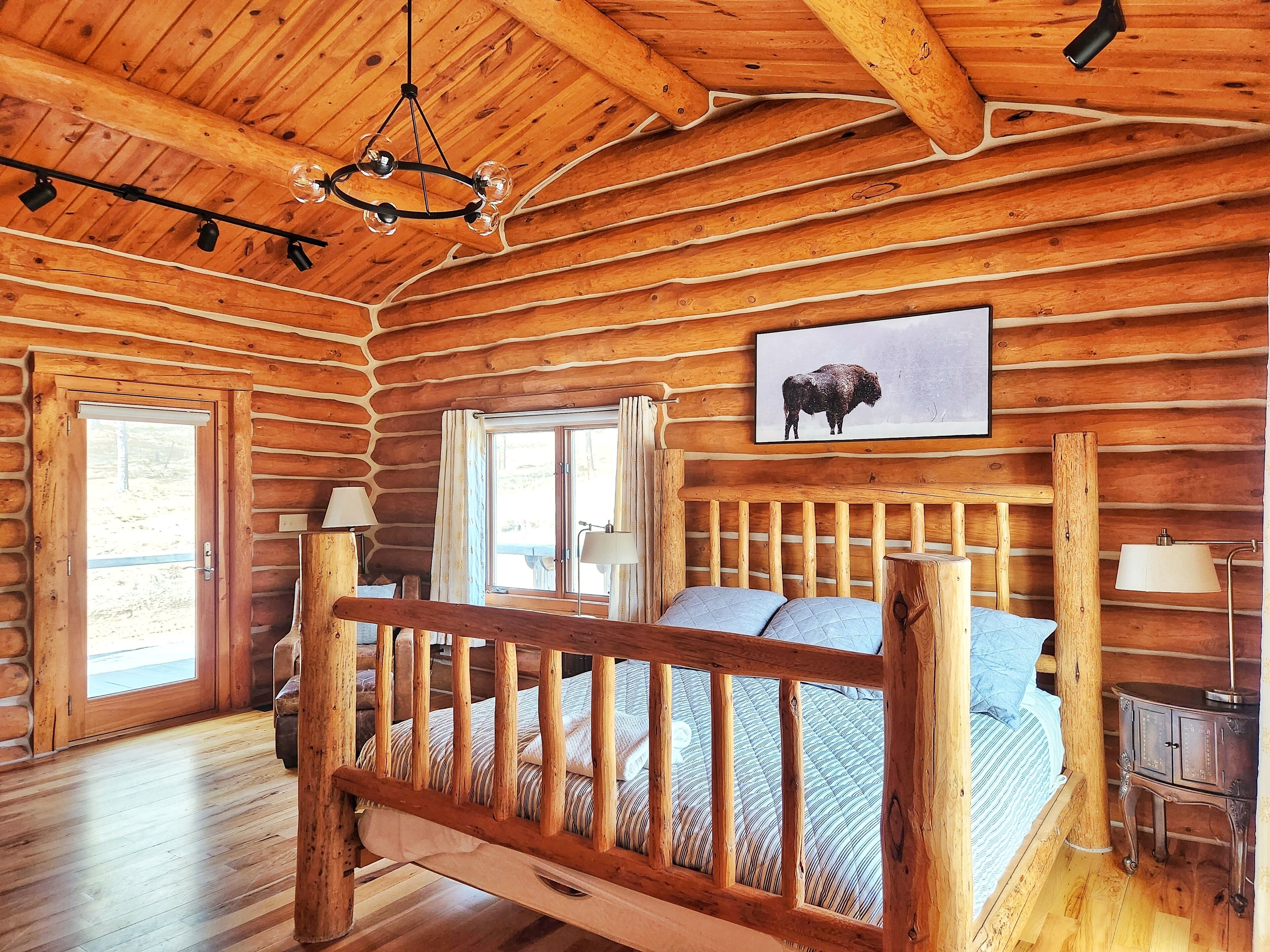 Une chambre dans une cabane en rondins, avec un lit en bois, un lustre et une fenêtre avec des rideaux.