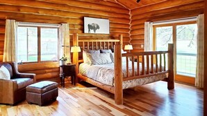 Un dormitorio de cabaña de troncos con una cama de madera, una silla, una mesita de noche y una ventana con vistas.