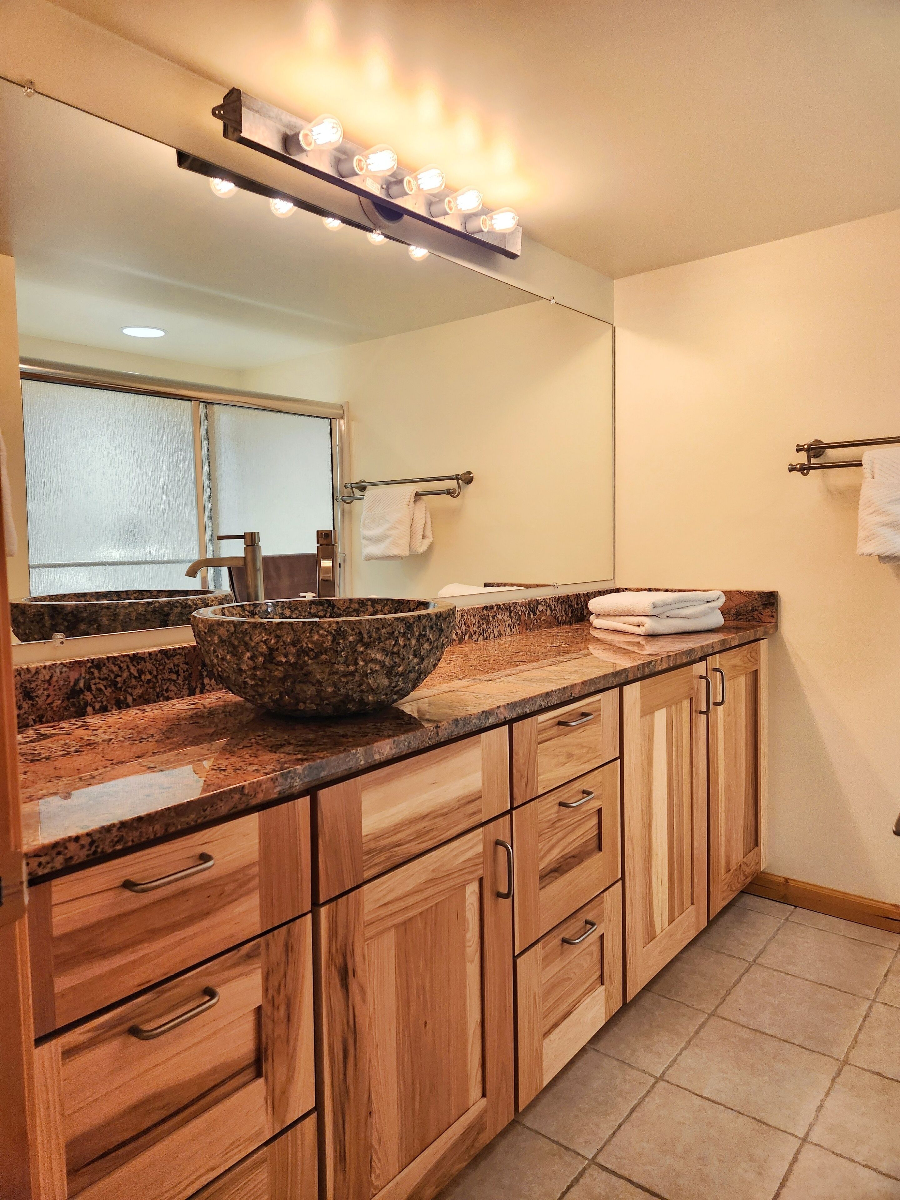 A bathroom with a granite countertop, a large mirror, and a vanity with wooden cabinets.