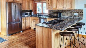 Una cocina amplia con armarios de madera, un refrigerador de acero inoxidable, encimera de granito y una isla grande con taburetes de bar.