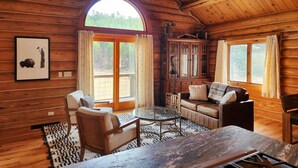 Interior acogedor de una cabaña de troncos con un amplio ventanal arqueado, muebles de madera y una araña.