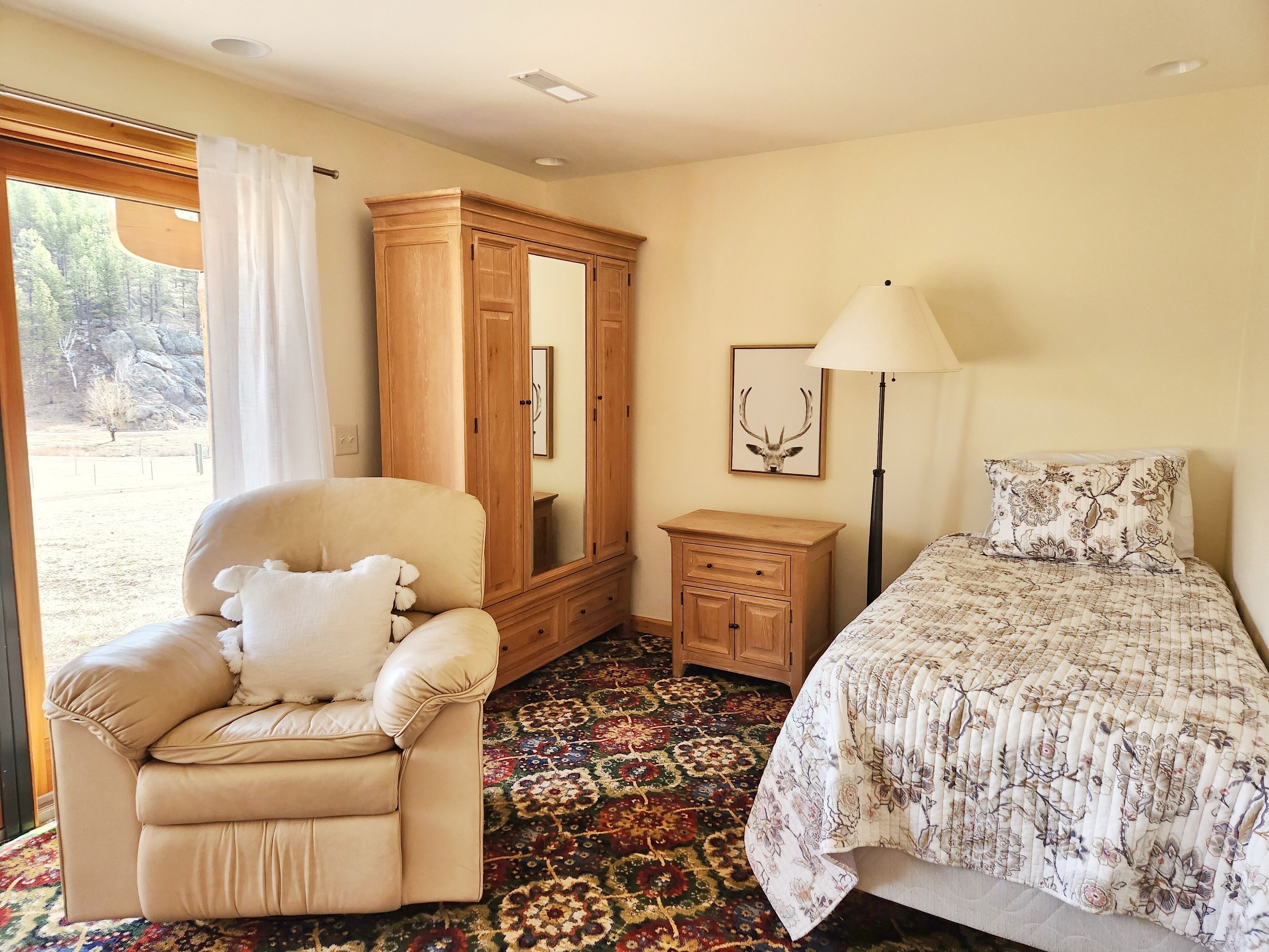 A bedroom with a bed, a chair, a wardrobe, a bedside table, a lamp, and a rug.