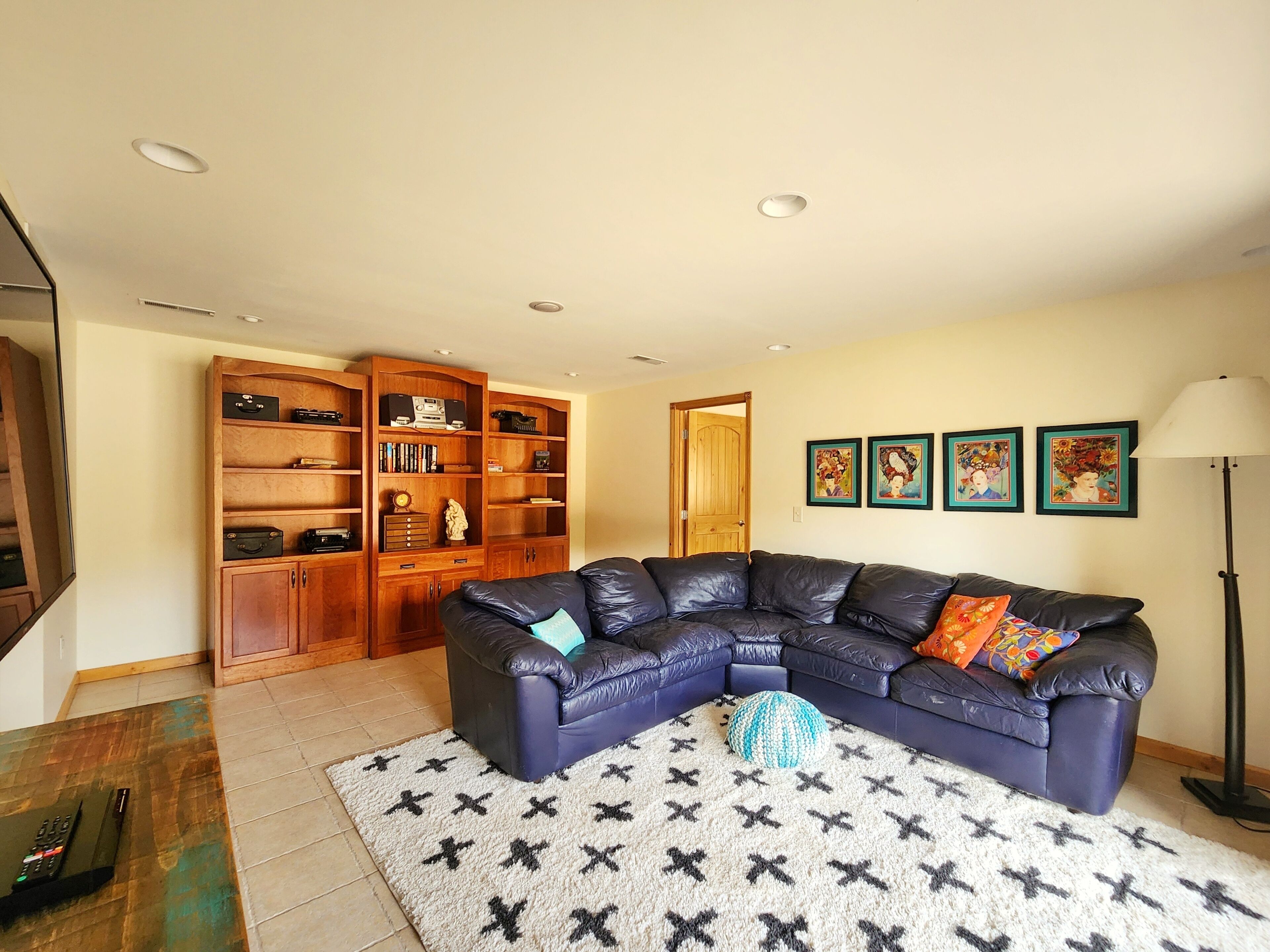A living room with a dark leather sectional sofa, a wooden bookcase, and a patterned rug.