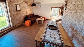 A rustic room with a stone wall, wooden floor, a sofa, a coffee table, and a dining table with a placemat. - Charming house in the heart of Burgundy, close to Beaune and the wine route. (Demigny)