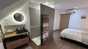 A modern bedroom with a wooden dresser, a round mirror, a bedside table, a bed with a white blanket, and a wall-mounted air conditioner. - Charming house in the heart of Burgundy, close to Beaune and the wine route. (Demigny)