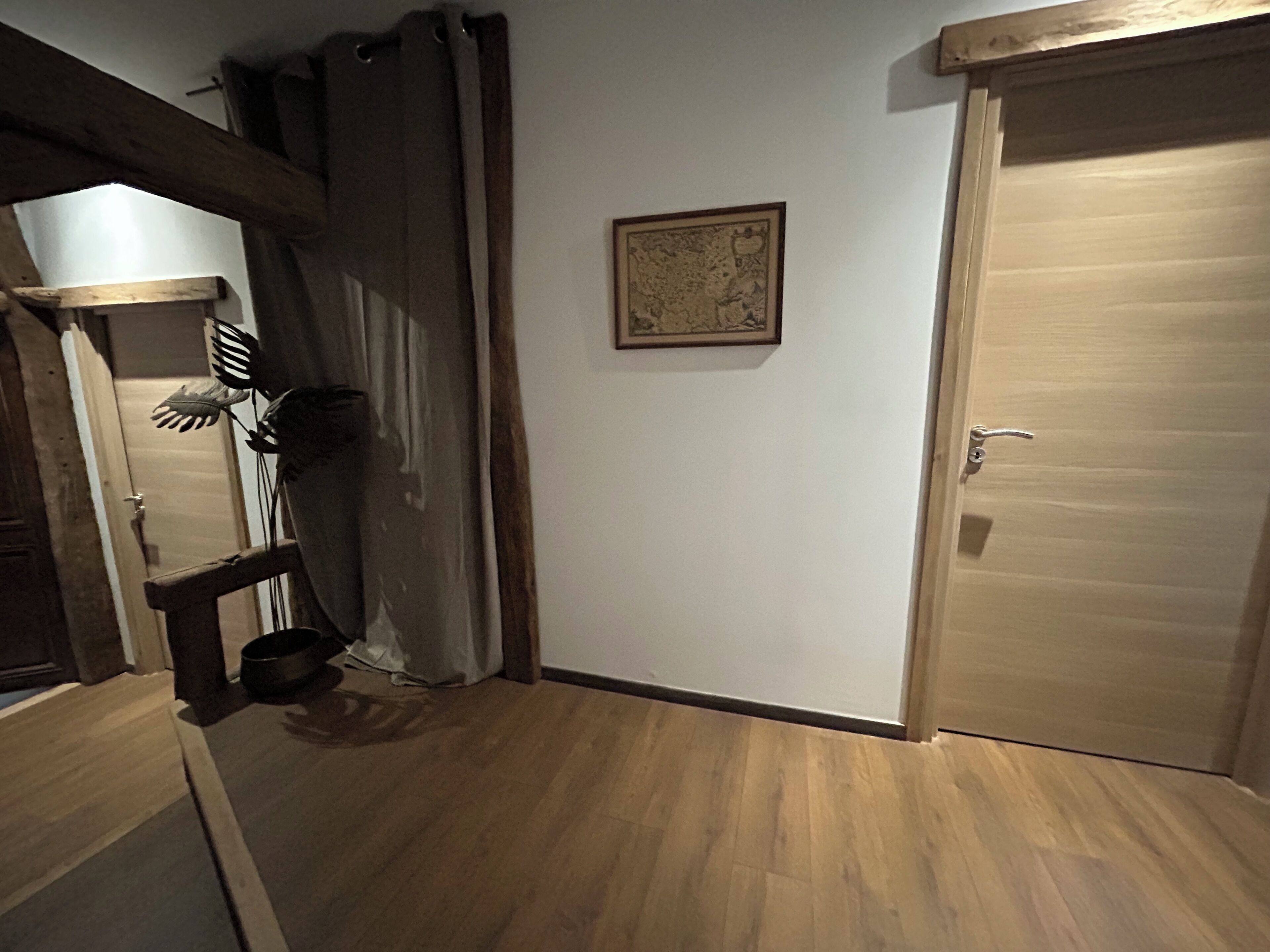 Een gang met houten vloer, een deur, een lijst met foto en een gordijn.