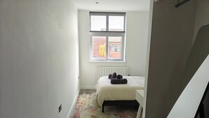 A small, bright room with a bed, a radiator, and a window. - Modern 1Br Sleeps3 - City Centre Location (Leicester)