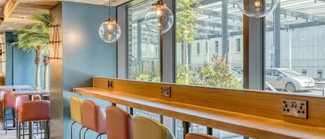 A modern bar area with wooden counters, colorful bar stools, and pendant lighting.