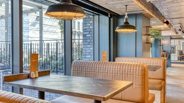 A restaurant with high ceilings, large windows, and leather booths. - Premier Inn London Paddington - Paddington Station (London)