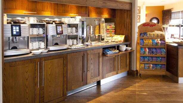 Un comptoir de petit-déjeuner avec des machines à café, un présentoir de céréales et une enseigne « Kellogg’s ».