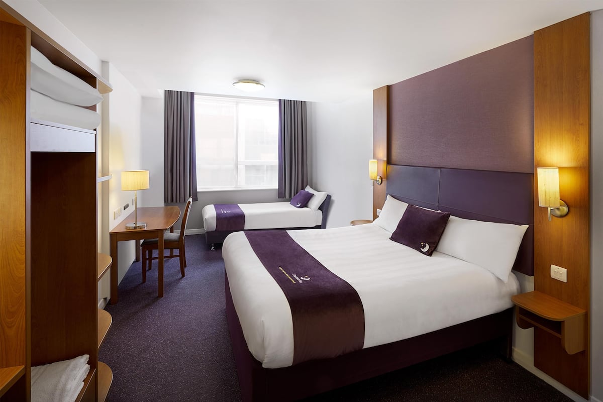 A hotel room with two beds, a desk, a chair, and a window with curtains.