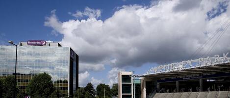 Un edificio moderno con un letrero de Premier Inn, fachada de vidrio y la entrada a un estadio con la indicación 'Wembley Park Station'.