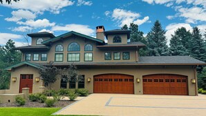 A large, two-story house with a spacious driveway, multiple garage doors, and a well-maintained lawn.