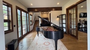 A spacious room with a grand piano, large windows, a staircase, and a gym area.