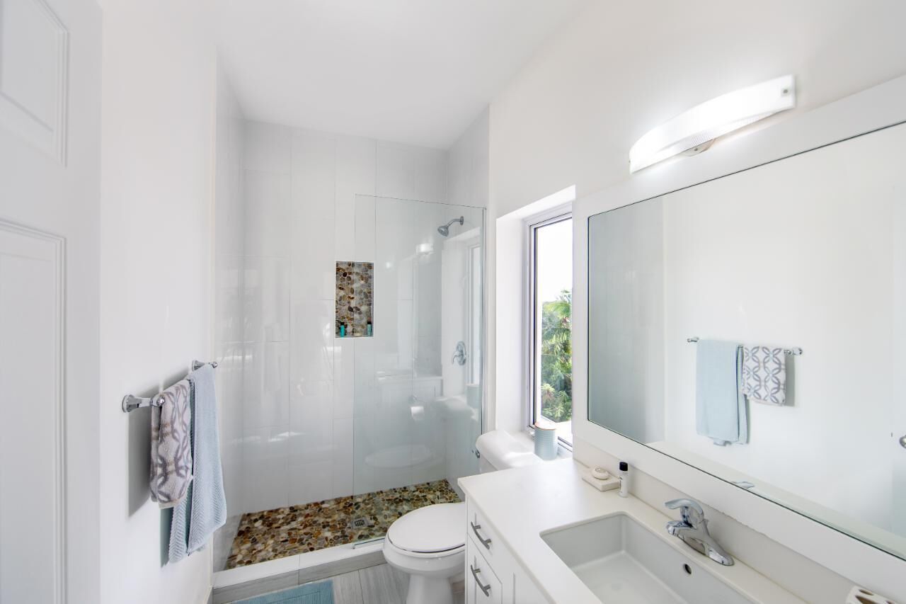 A modern bathroom with a glass-enclosed shower, a white toilet, a large mirror, and a granite countertop sink.