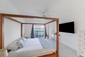 Quarto com cama de dossel, escrivaninha, cadeira, televisão e varanda com vista.